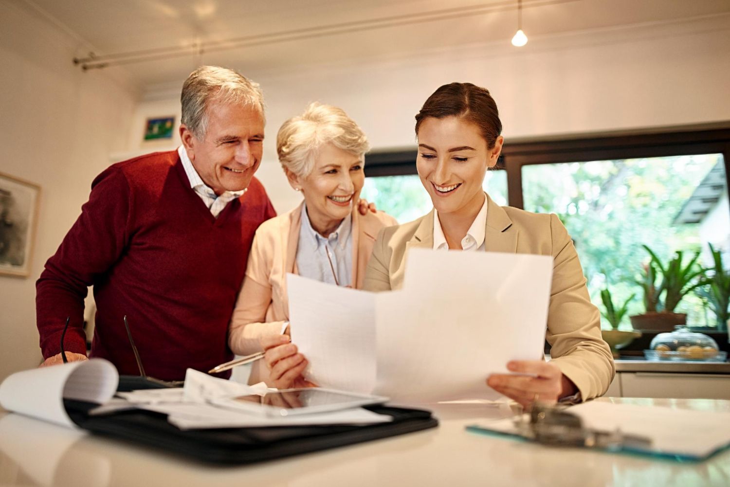 Three people review documents together at a desk in a bright office, smiling and focused.