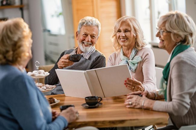 Group of older adults chatting at a café table with drinks and a menu booklet