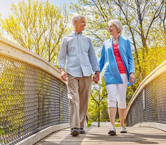 Two people walking on a bridge, smiling, with spring trees in the background.