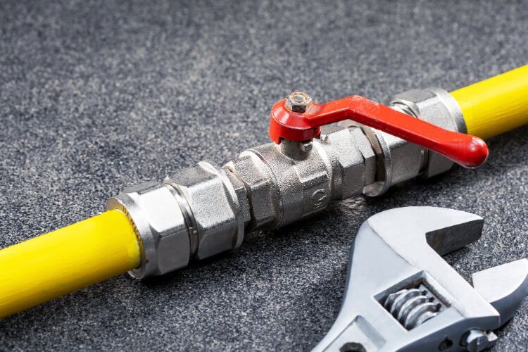 Yellow gas pipe with valve and wrench on a gray surface.