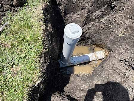 Gray pipe in an earthen ditch, with a white cap, near green grass.