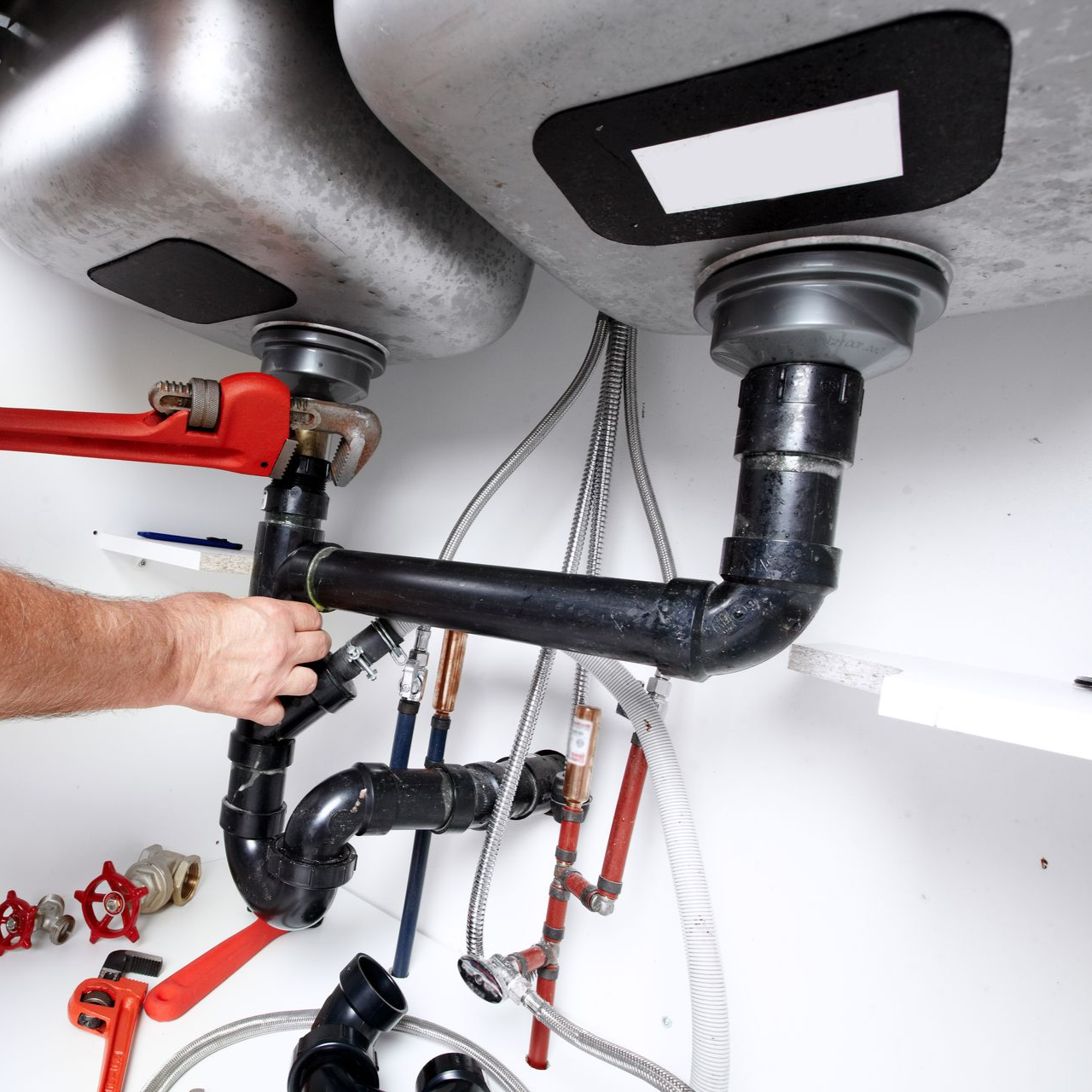 Plumber working under a kitchen sink, using a wrench to tighten pipes.