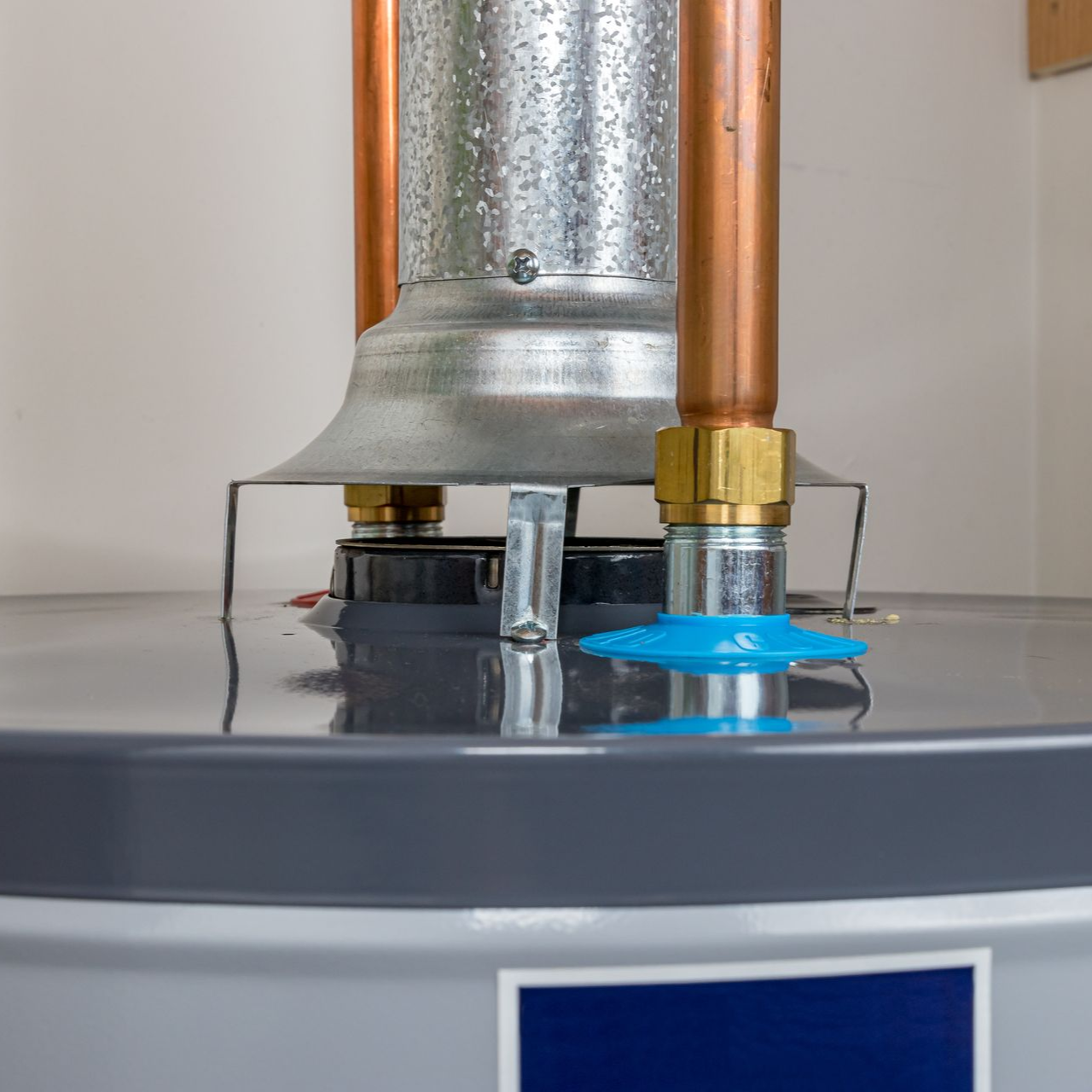 Close-up of a water heater, showing copper pipes and the top of the tank with a blue drain tube.