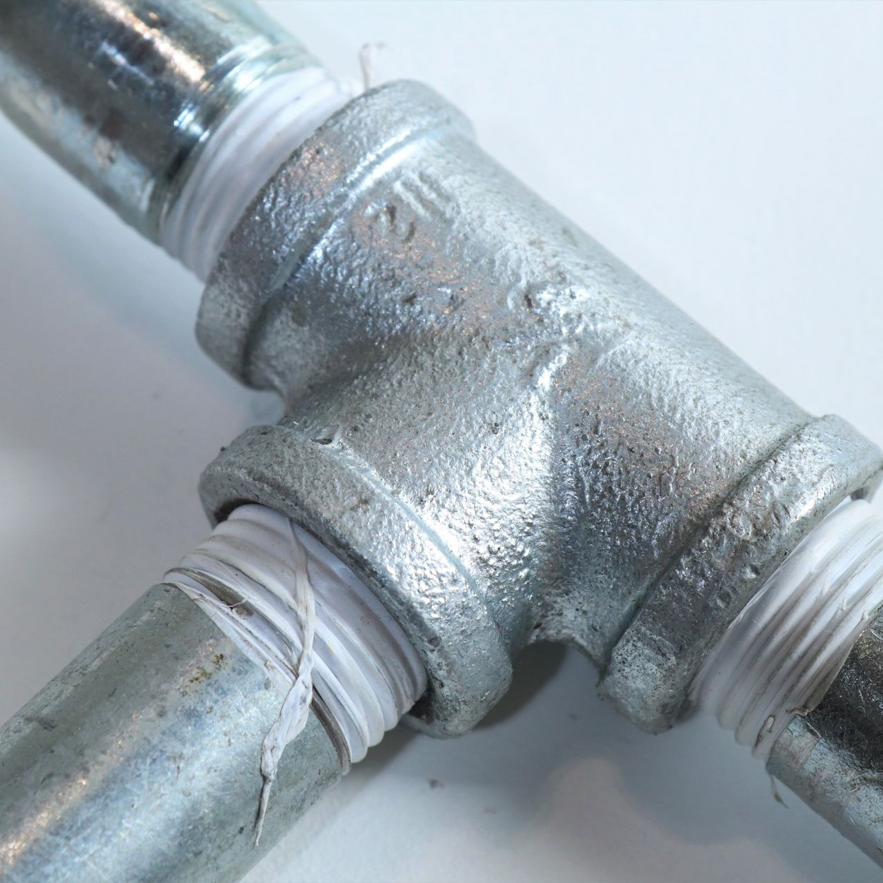 Galvanized steel pipe fittings with white thread seal tape.