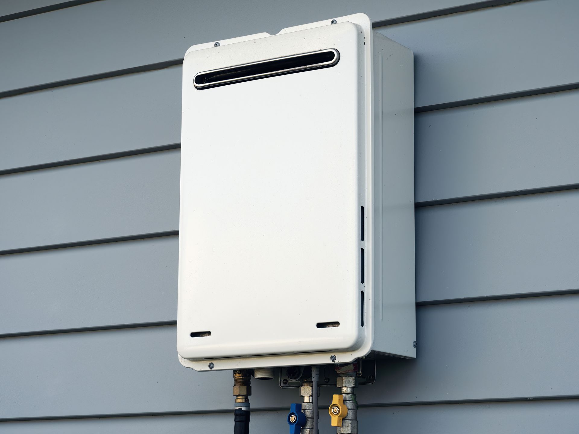 White tankless water heater mounted on a gray siding wall.