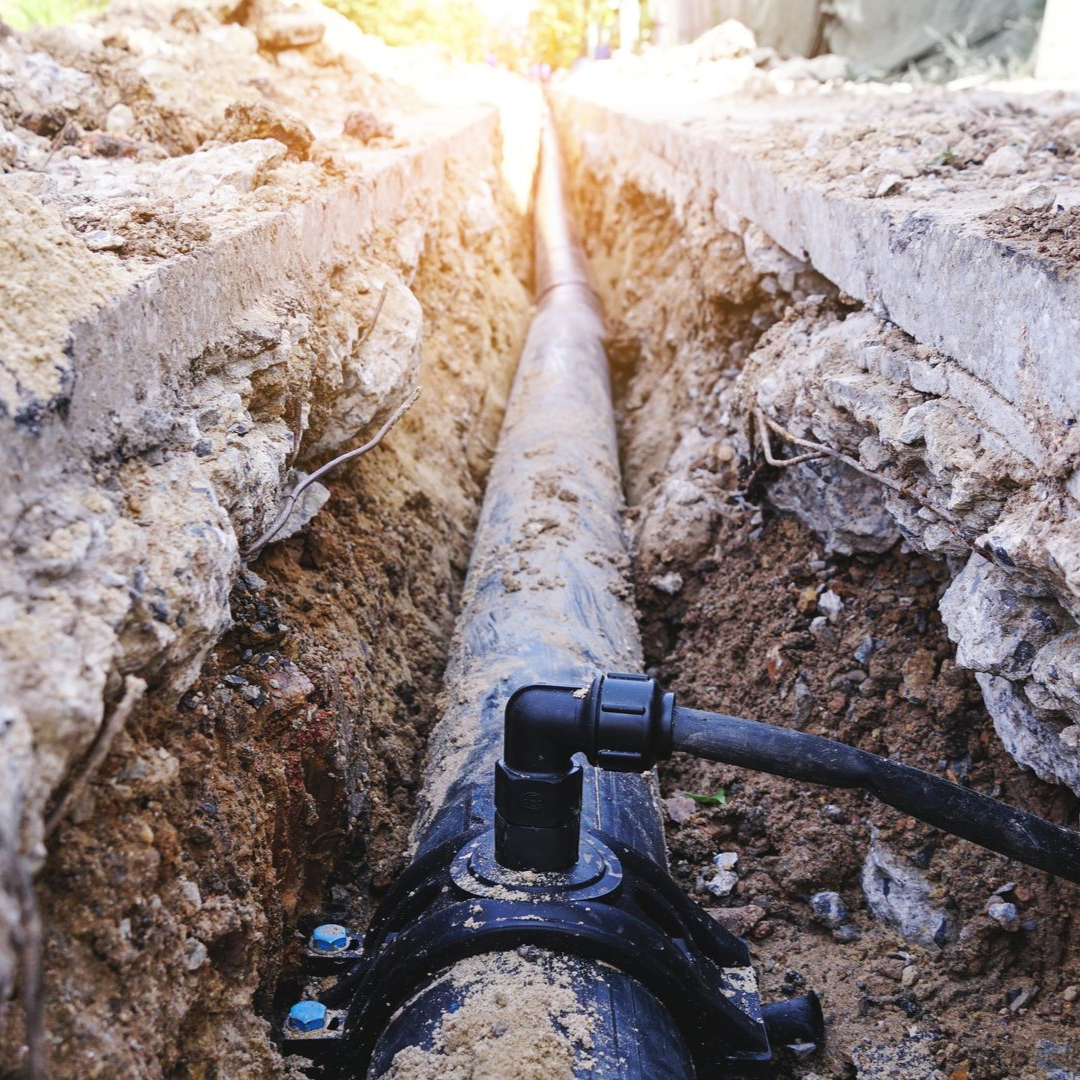Trench with a black pipe and fittings, exposed during utility repair, in an outdoor setting.