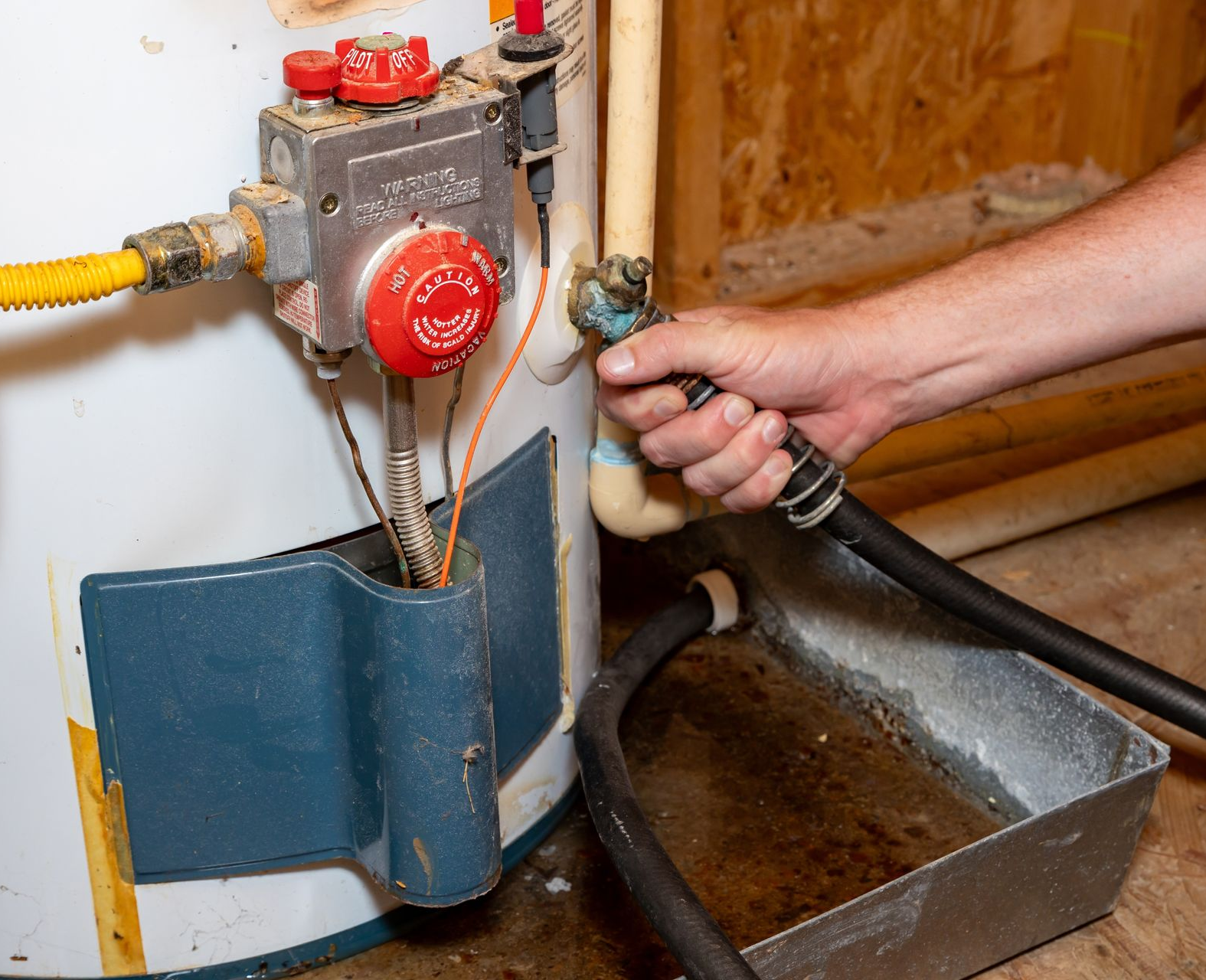 Hand draining a water heater, black hose into a tray.