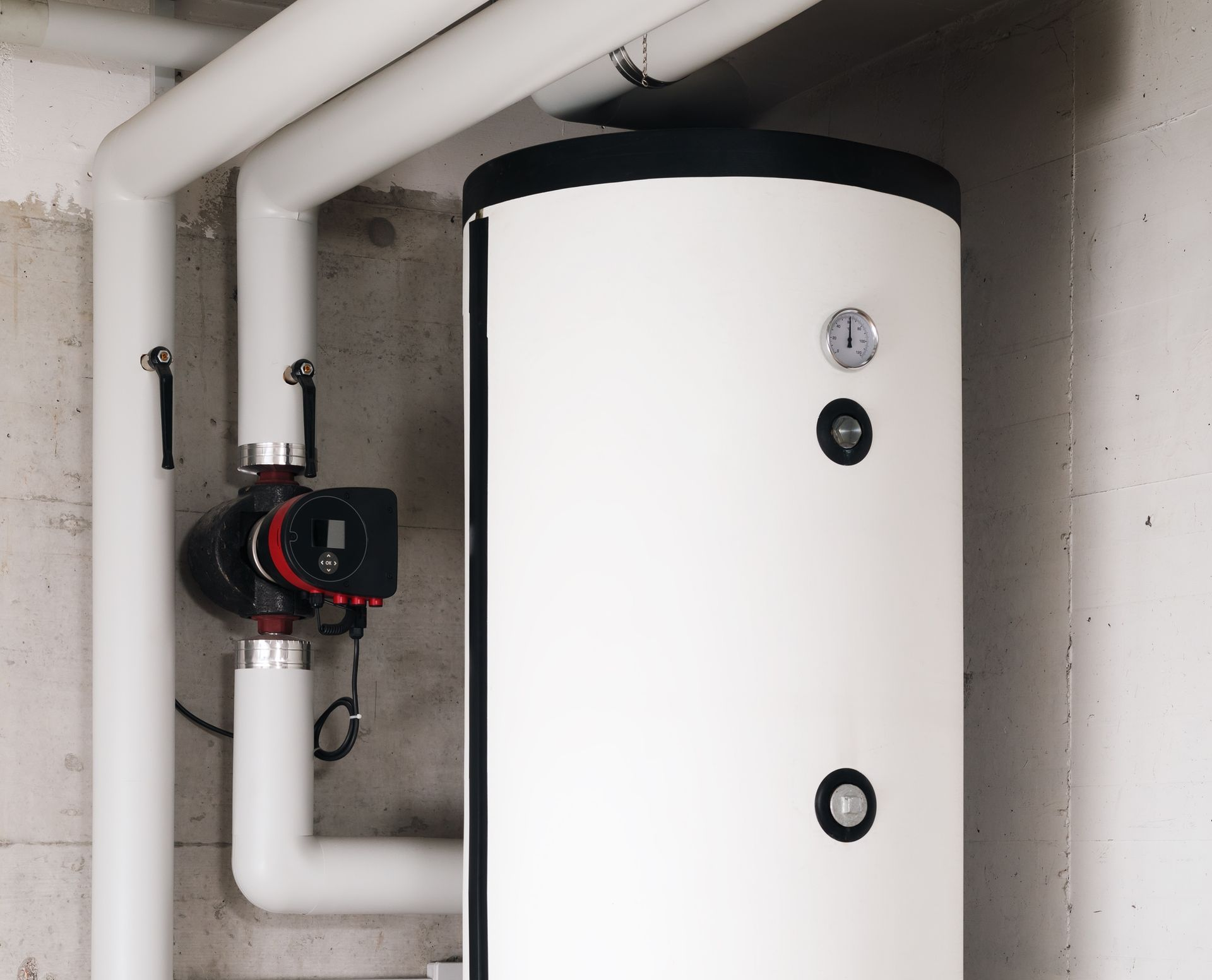 White water heater with pipes, a pump, and gauges, in a basement setting.