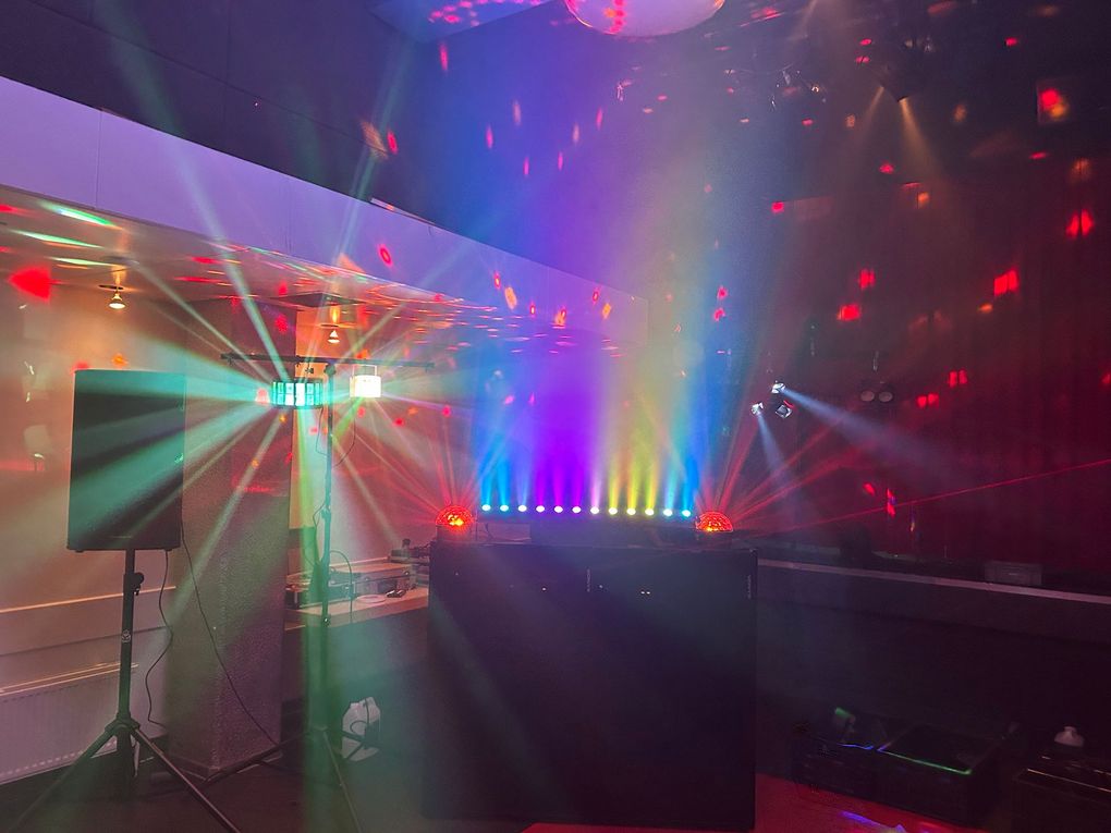 Een kleurrijke lasershow in een schemerige zaal met stralen, rook en regenboogkleuren op de vloer.