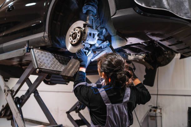 Mechanic working on car brakes under a vehicle lift in a repair shop.