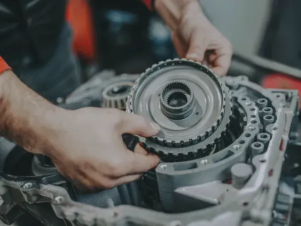 Hands assembling a car transmission, holding gears. Workshop setting, mechanical work.