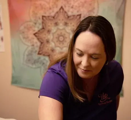 A woman in a purple shirt is giving a massage to another woman.
