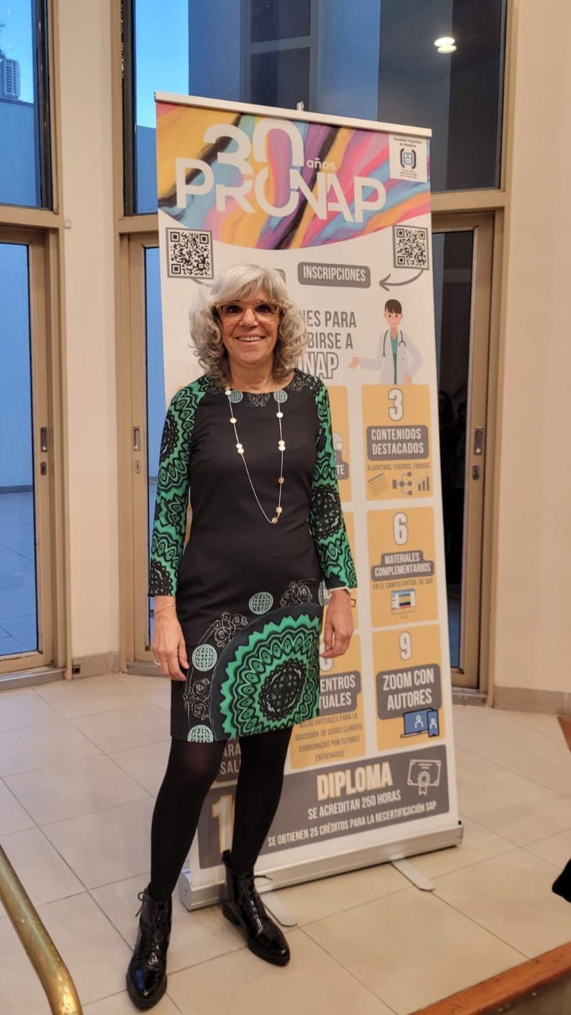 Una mujer con vestido está de pie junto a una pancarta. La pancarta tiene texto y el dibujo de una persona.