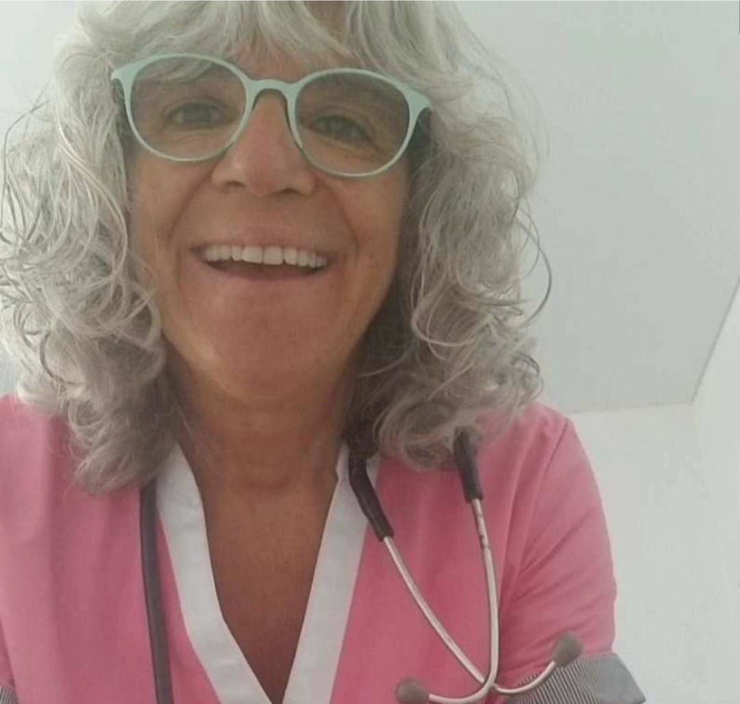 Mujer con gafas y uniforme médico rosa, sonriendo y con un estetoscopio alrededor del cuello.