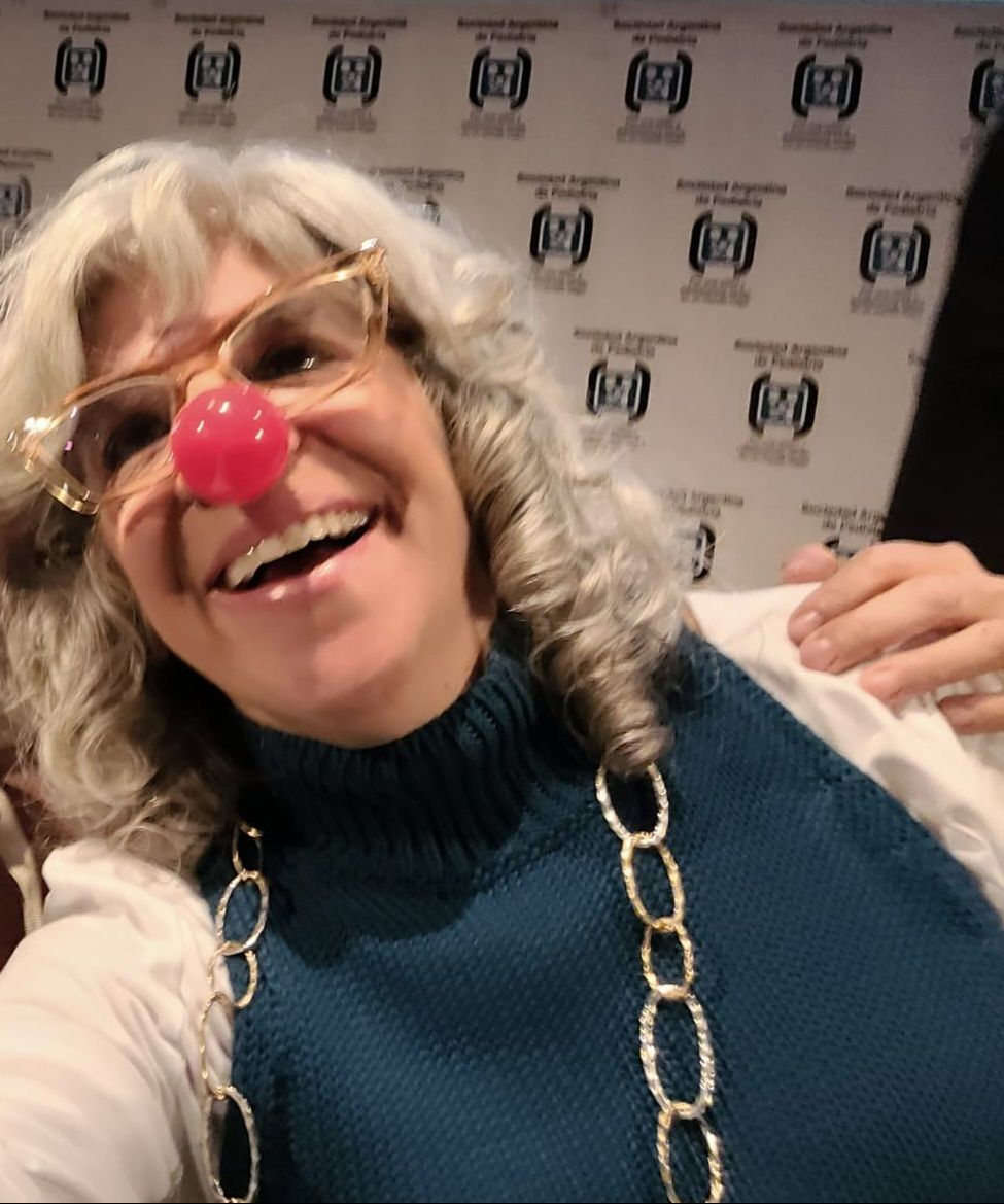 Mujer con cabello gris y gafas que lleva una nariz roja de payaso, riendo.