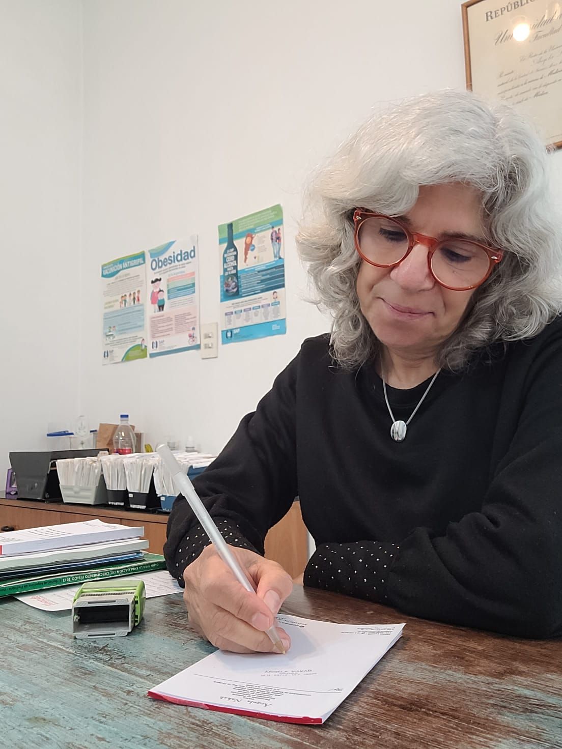 Mujer escribiendo en un escritorio, usando gafas, en un entorno de oficina.