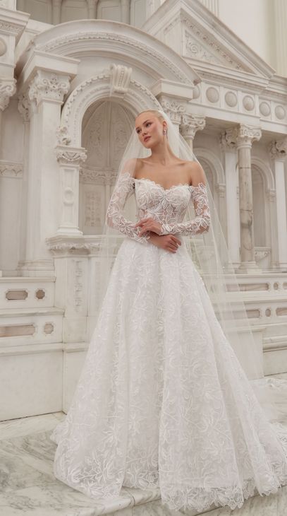 Woman in a white sequined gown standing before an ornate white building, holding flowers.