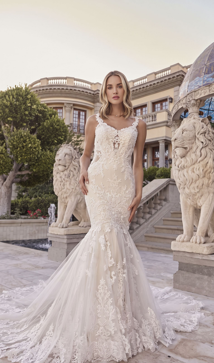 Woman in a white lace gown standing on palace steps between stone lion statues at dusk
