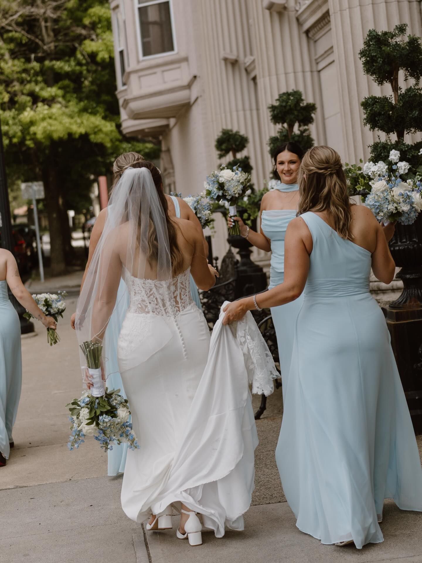 Bridal party walking outdoors, with a bride in a white gown and bridesmaids in light blue dresses