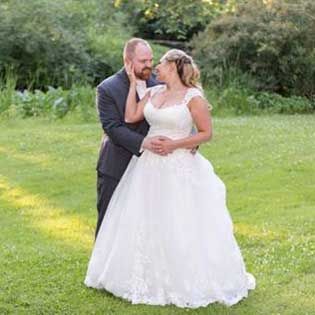 Bride and groom embracing in a grassy outdoor setting, with the bride in a white gown and the groom in a dark suit