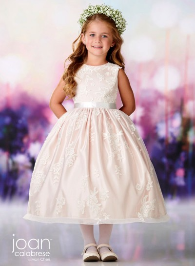 Girl in a white dress with a floral crown, standing against a soft pastel background.