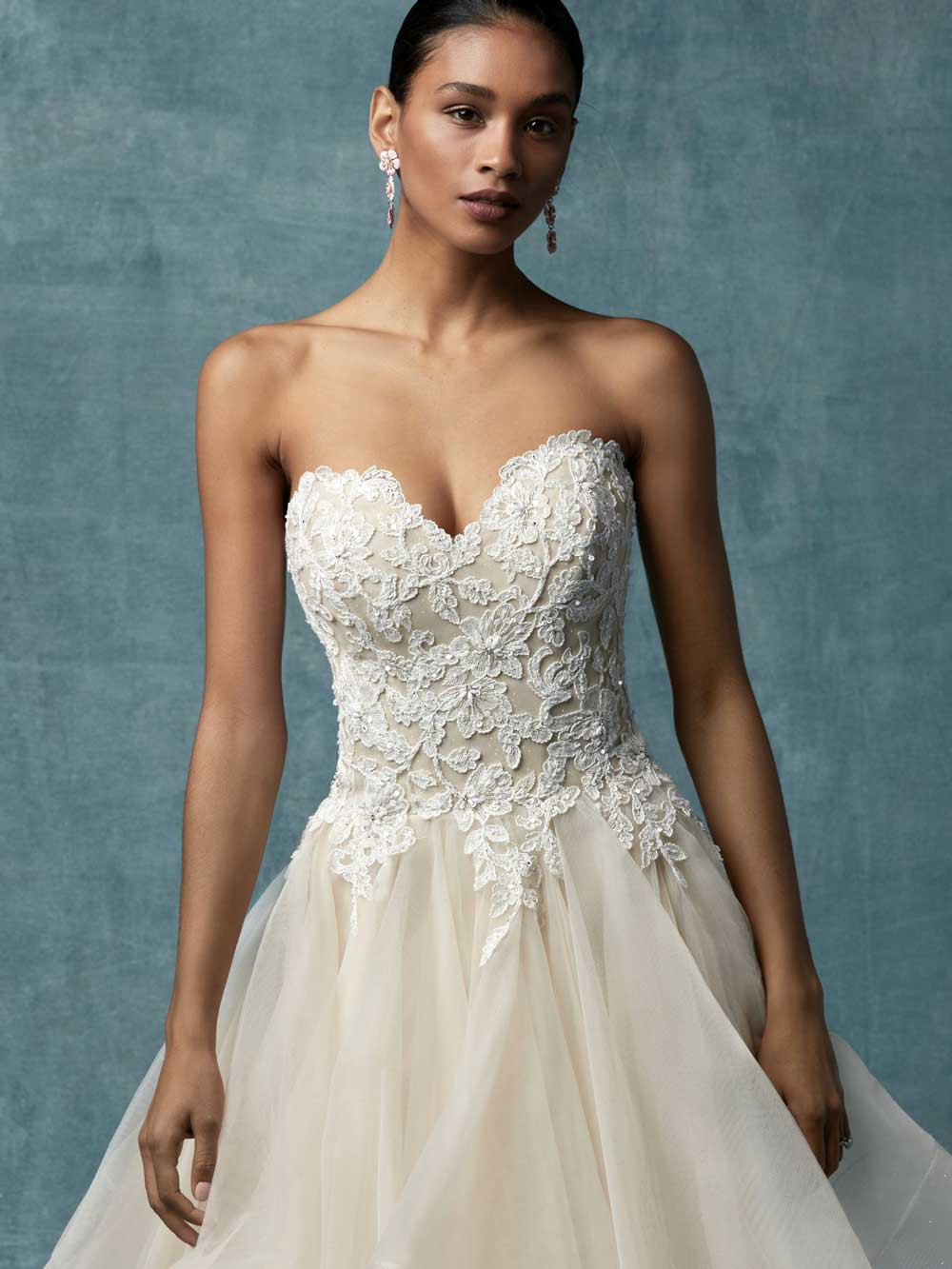 Bride in a strapless ivory lace wedding gown with a flowing tulle skirt, standing against a gray backdrop