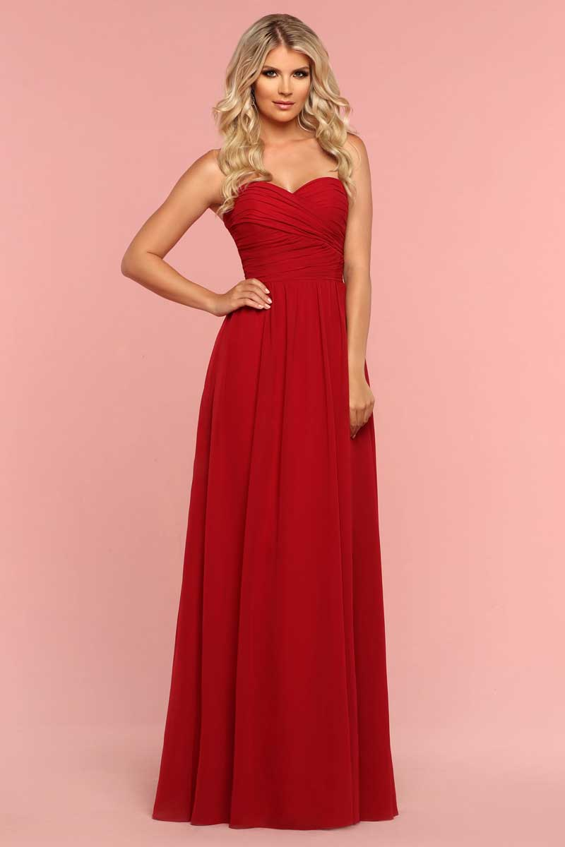 Woman in a red strapless gown posing against a pink background.