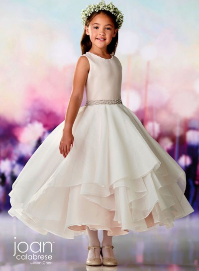 Young girl in a white dress and floral crown, standing against a pastel background.