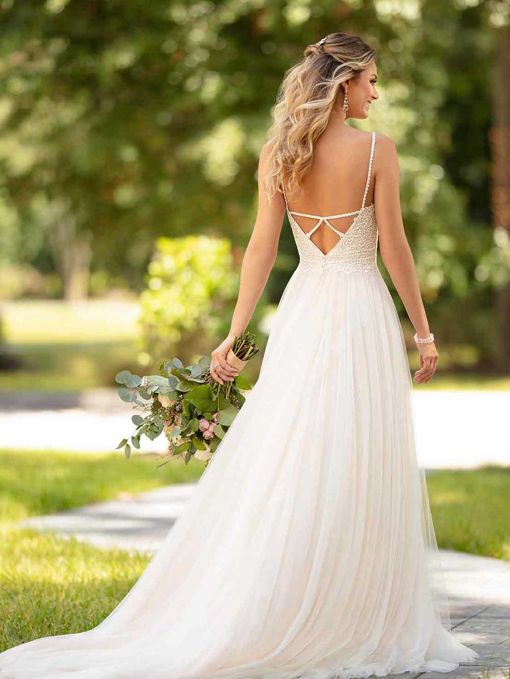 Bride in a white lace-back gown holding a bouquet outdoors on a sunlit path