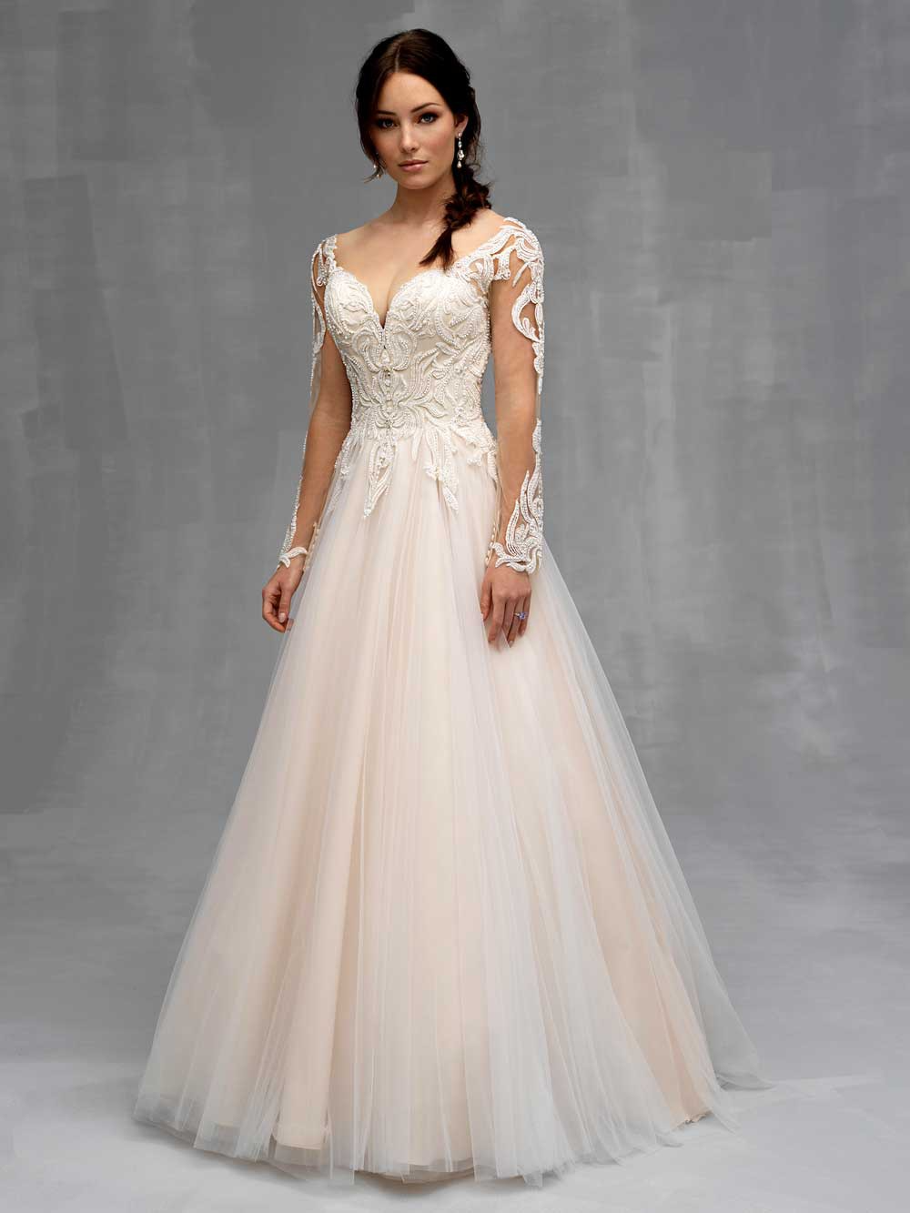 Woman in a white lace wedding gown standing against a gray studio backdrop.