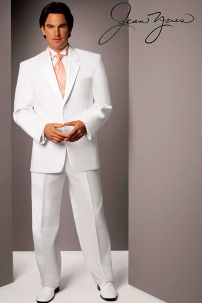 Man in a white suit standing in a gray studio backdrop with signature at top right