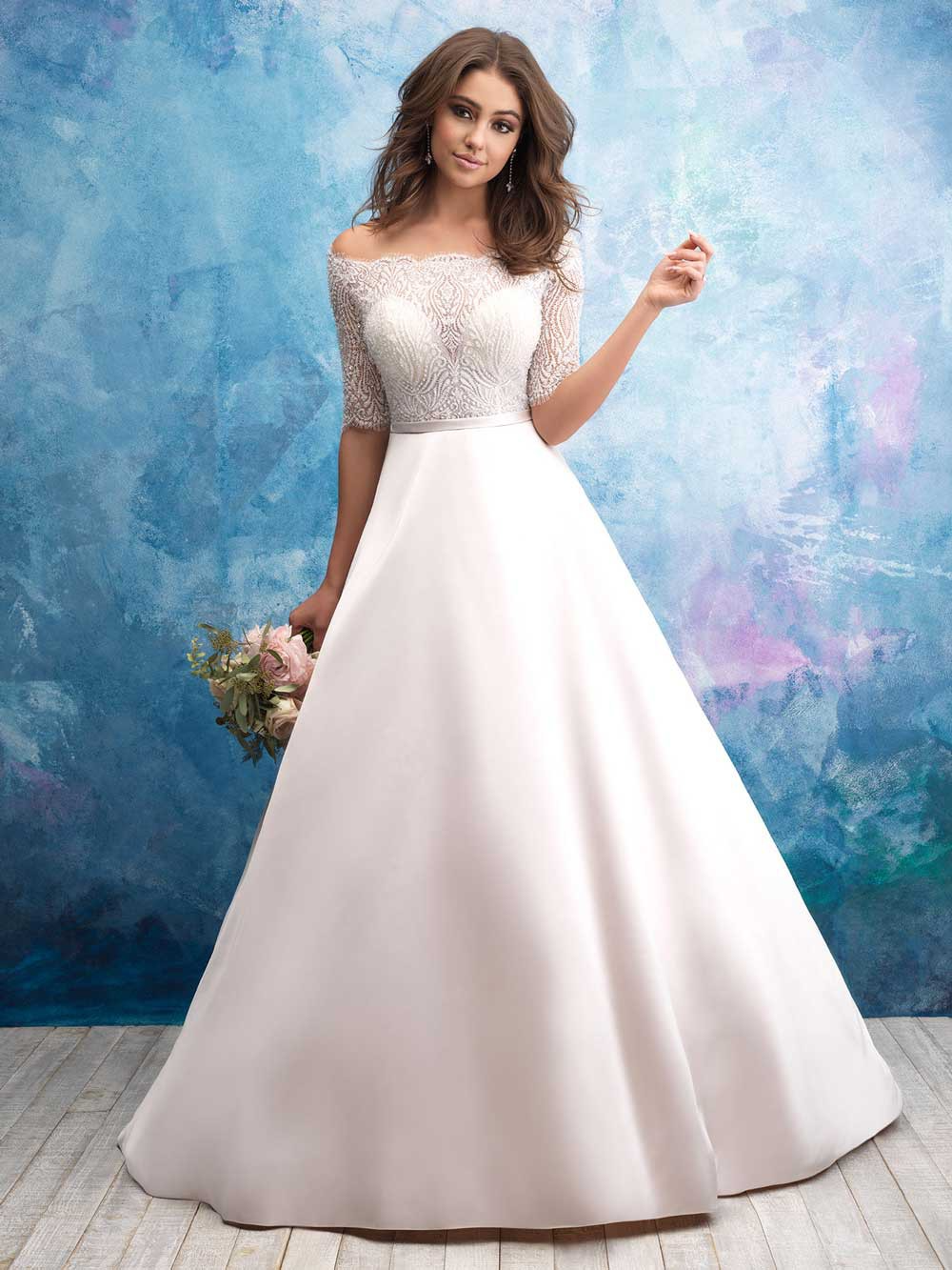 Woman in a white bridal gown standing against a blue backdrop, holding a bouquet.