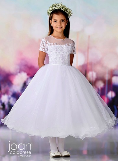 Young girl in a white floral dress and tiara, standing against a soft pastel background.