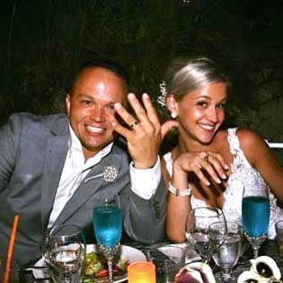 Smiling couple at a dinner table, the man showing a ring with his hand raised, blue drinks in front.