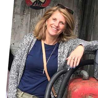 Smiling woman in a navy shirt and gray cardigan leaning on a red tractor indoors