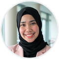 Smiling person wearing a black hijab and a light pink blazer, centered in a circular frame against a blurred background.