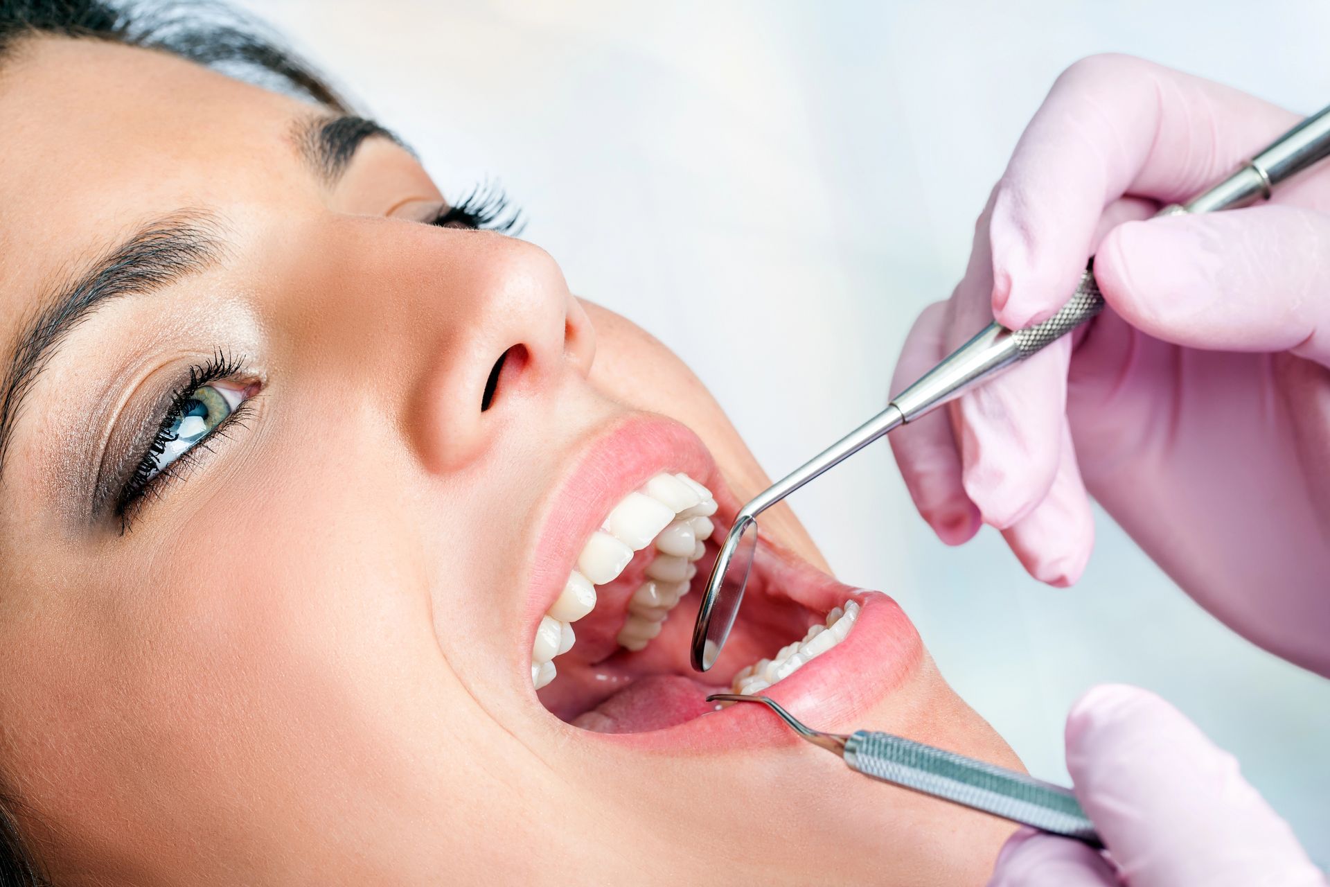 Dentista che esamina la bocca aperta del paziente con uno specchietto e uno strumento, indossando guanti rosa
