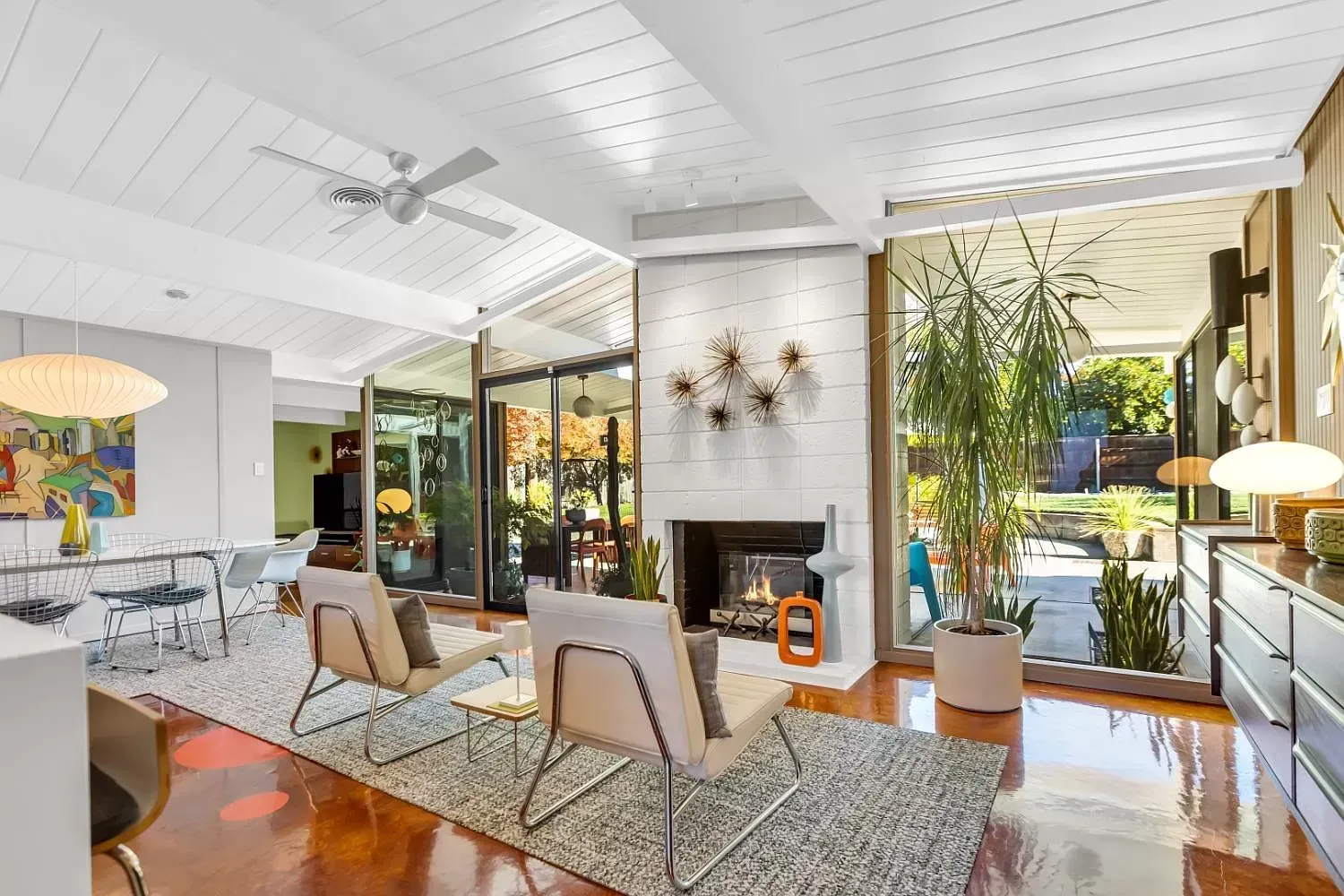 Bright modern living room with white walls, fireplace, glass doors, and patterned seating overlooking a pool. | Beth Ellinthorpe Realtor | Luxury Real Estate