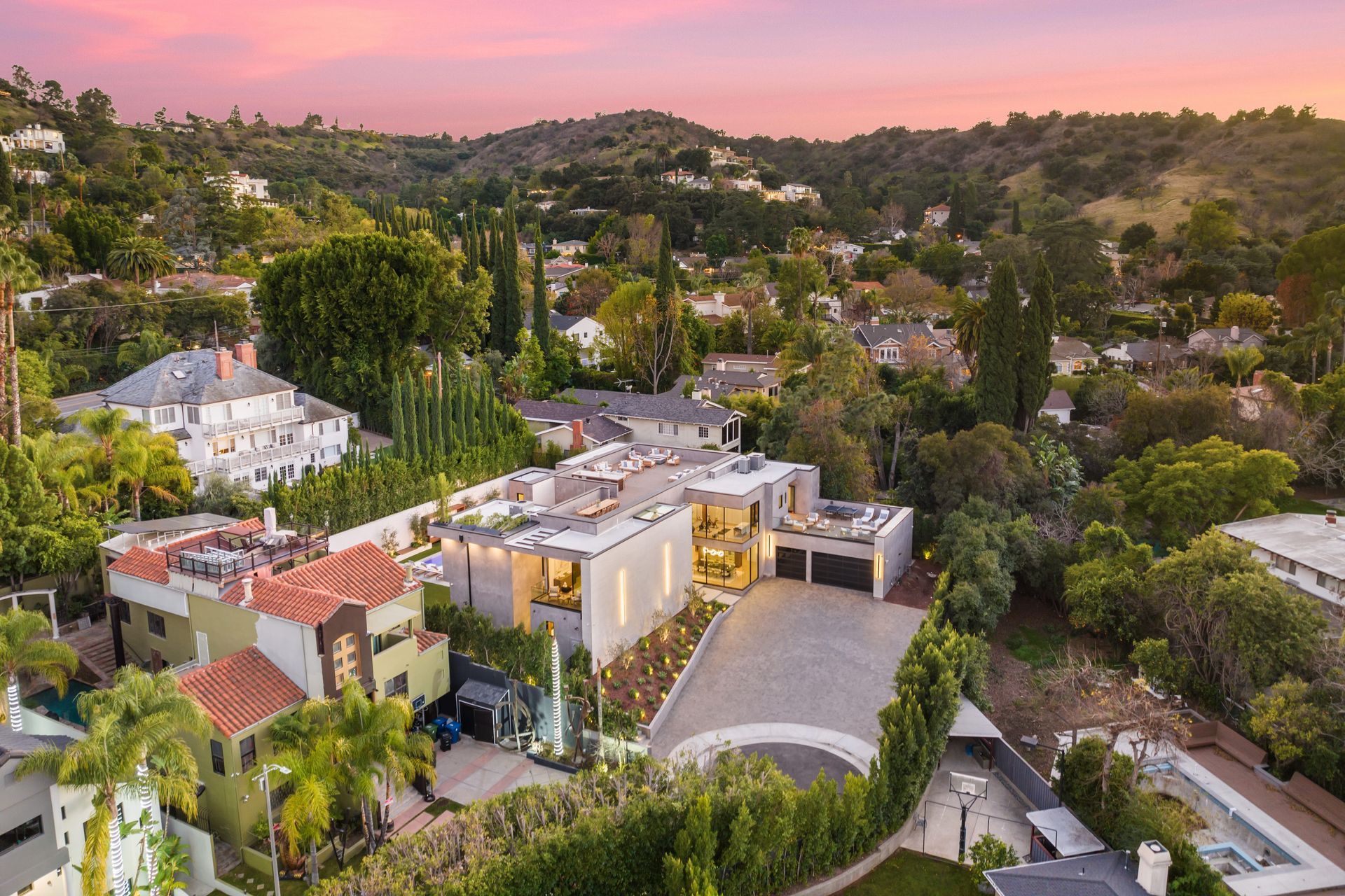 Aerial view of hillside homes and lush trees at sunset under a pink sky Beth Ellinthorpe Realtor | Luxury Real Estate