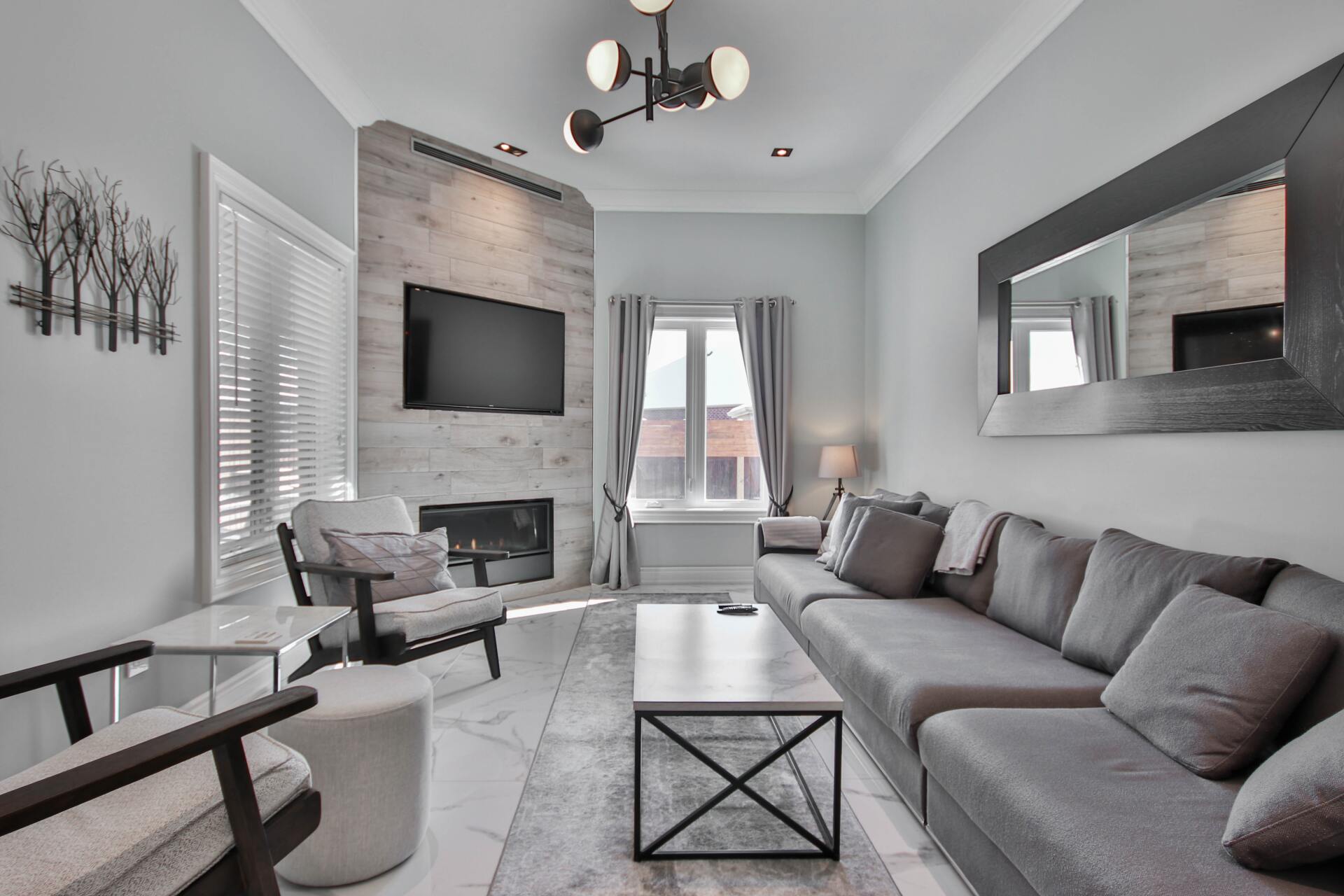 Modern gray living room with sectional sofa, wall-mounted TV, fireplace, and large mirror. | Beth Ellinthorpe Realtor | Luxury Real Estate