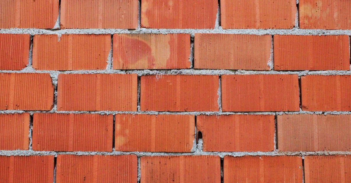 Bricklayer in a yellow hard hat, laying bricks with a hammer, building a wall.