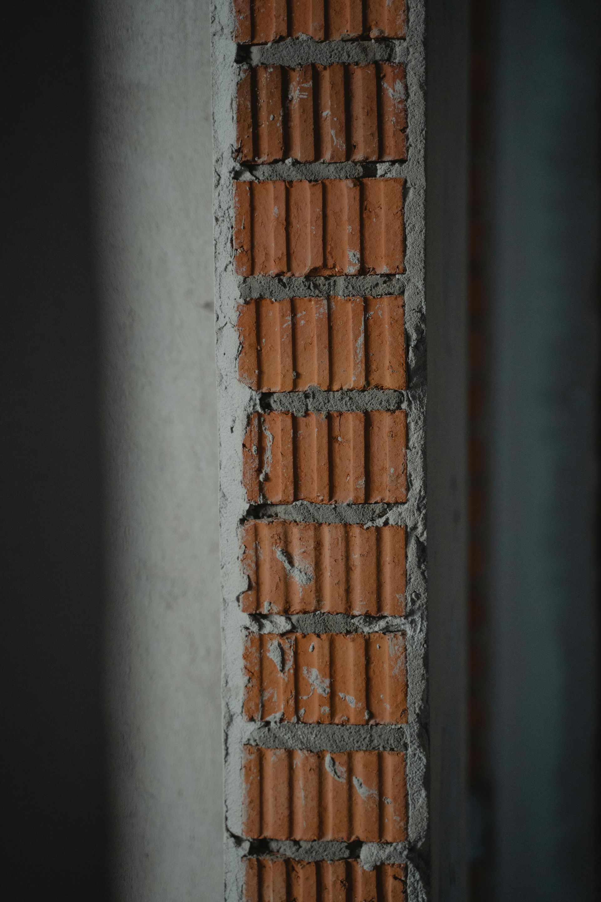Exposed brick column, alternating with a concrete wall, in an interior space.