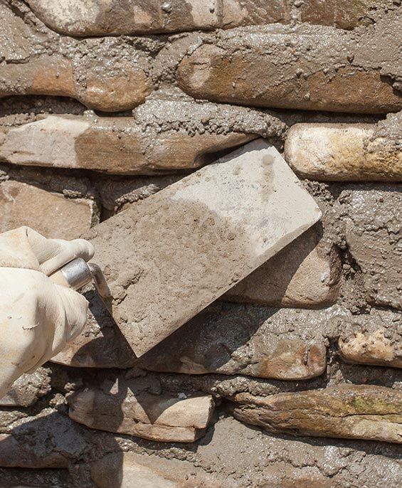 Bricklayer in a yellow hard hat, laying bricks with a hammer, building a wall.