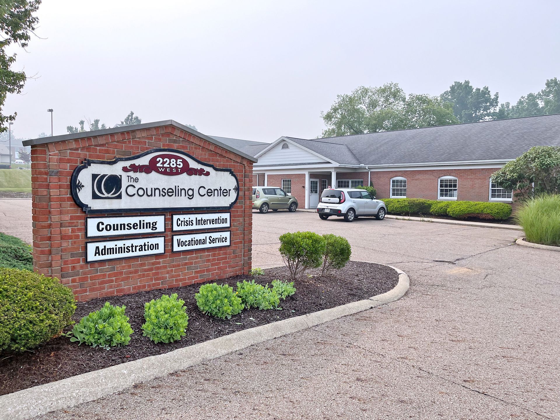 Sign for The Counseling Center in front of a brick building. Cars in the parking lot. Overcast day.