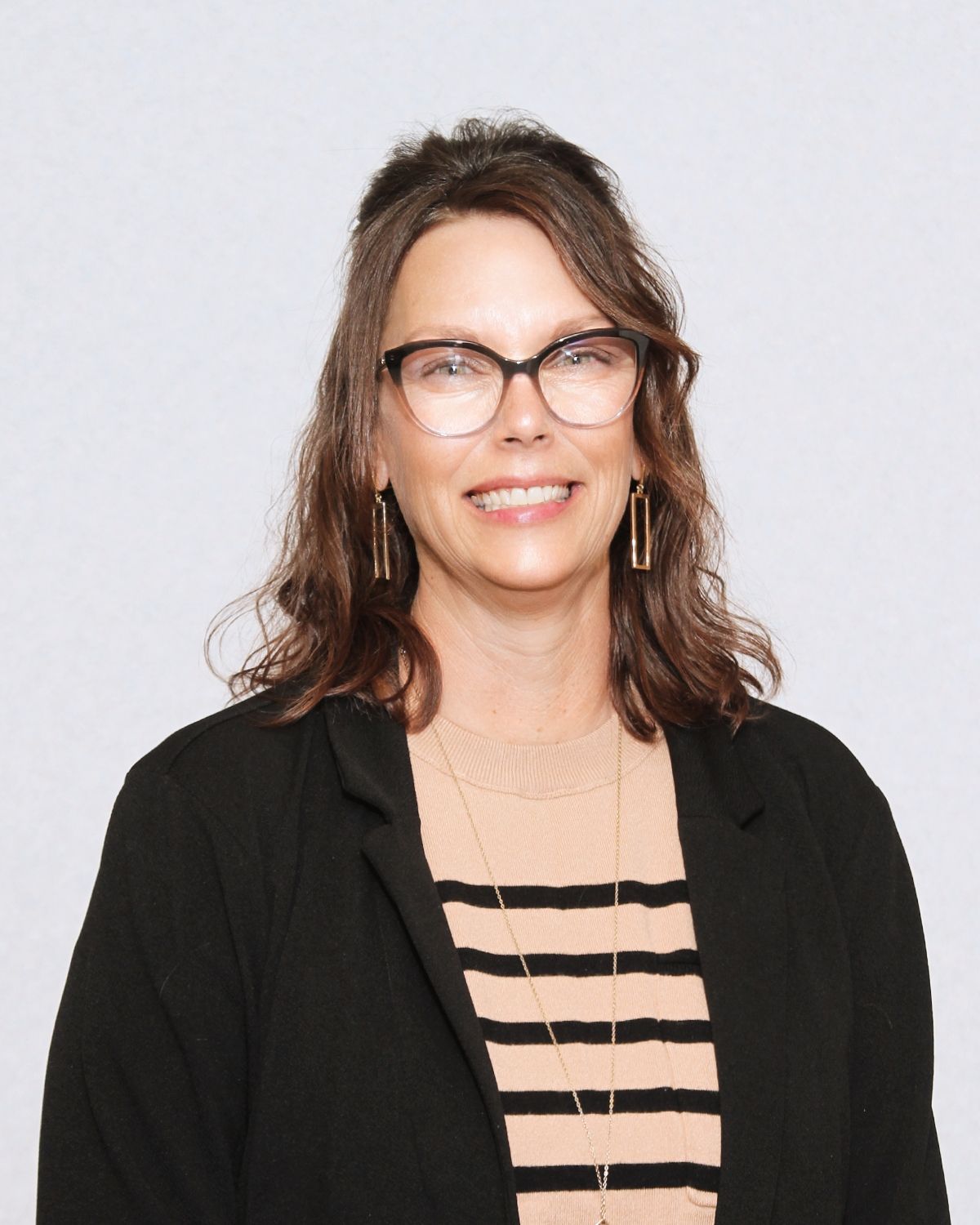 Woman wearing glasses and a blazer smiles at the camera.