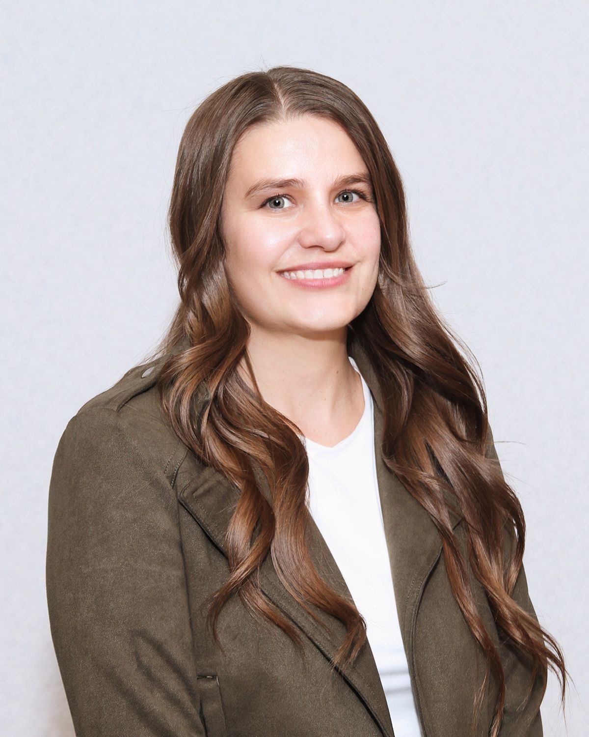 Woman with long brown hair smiles, wearing a green blazer over a white shirt.
