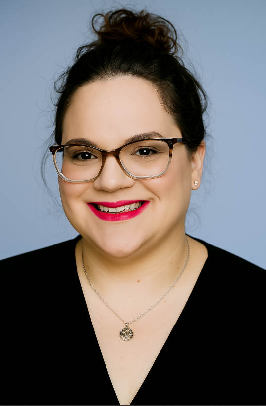 Woman smiling, wearing glasses and black top, hair in a bun, red lipstick.