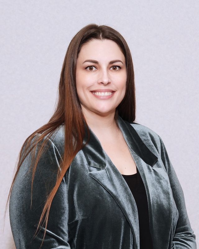 Woman with long brown hair smiling, wearing a teal velvet jacket, in a studio setting.
