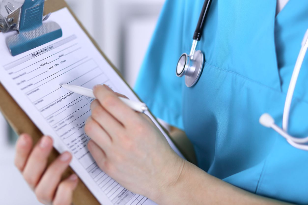 A doctor is writing on a clipboard with a pen.