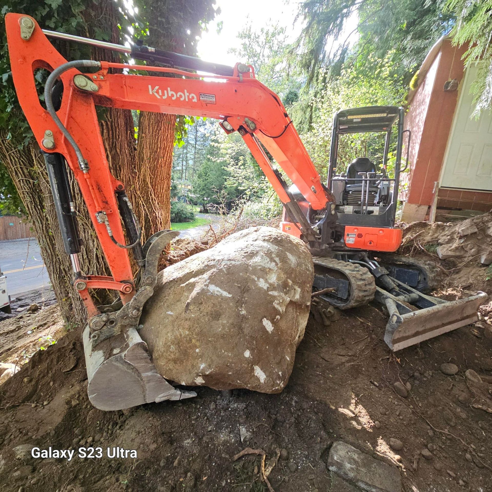 An orange excavator is digging a large rock in the dirt.